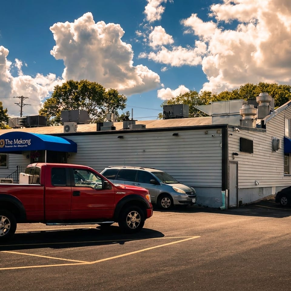 The Mekong restaurant exterior with a blue awning, parked cars, and a bright cloudy sky.